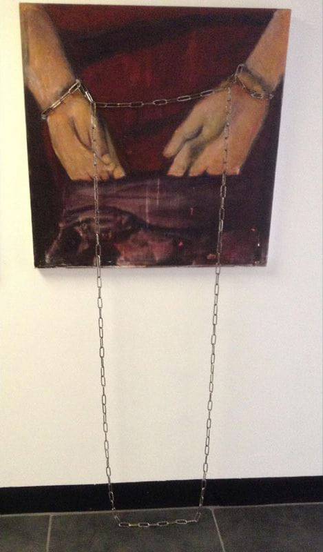 Gallery wall painting of tan hands bound by chain against maroon, with real metal chains draping onto a tiled floor