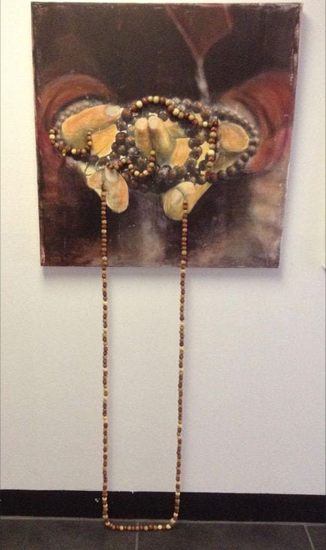 Square painting of cupped hands holding mala beads; real bead strands hang down to dark floor, ochre and brown tones