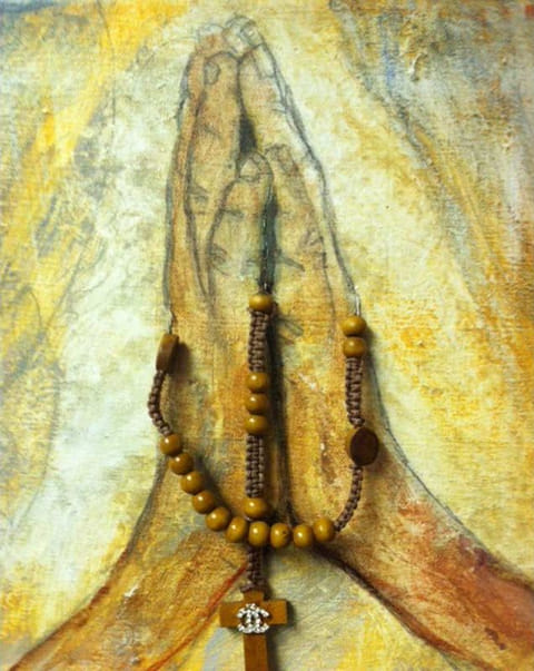 Painted praying hands in golden ochre and cream with a real wooden rosary and cross affixed across the canvas